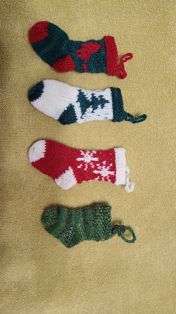 Four wee ornament socks white with a green intarsia tree, freen with a red intarsia cardinal, red with two white intarsia snowflakes and a green striped one.